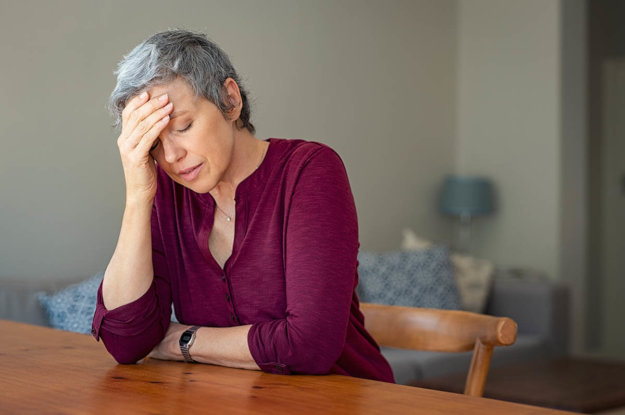 senior woman sitting at table holding head experiencing oxycontin side effects