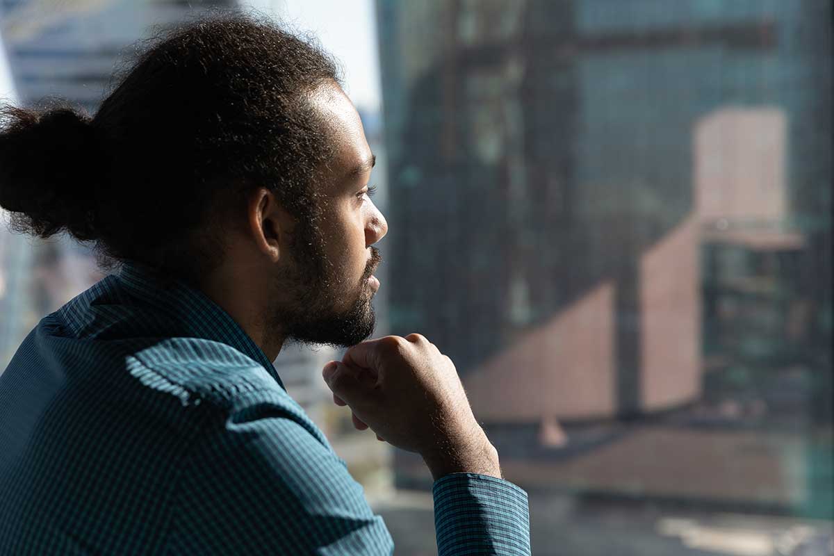 Bearded man looking out window considering short-term addiction treatment