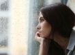 Woman staring out of rainy window reflecting on alcohol and depression