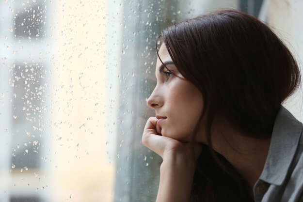 Woman staring out of rainy window reflecting on alcohol and depression