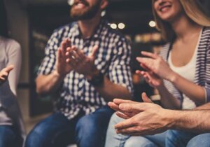 Individuals in a non-12-step program smiling and clapping as they sit in a supportive circle