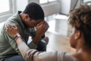 Man in PTSD treatment program with head in hands is comforted by therapist
