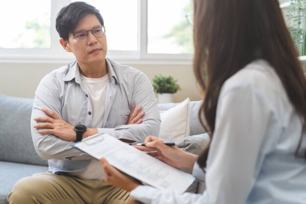 Man listening thoughtfully to a therapist taking notes during a substance use treatment session