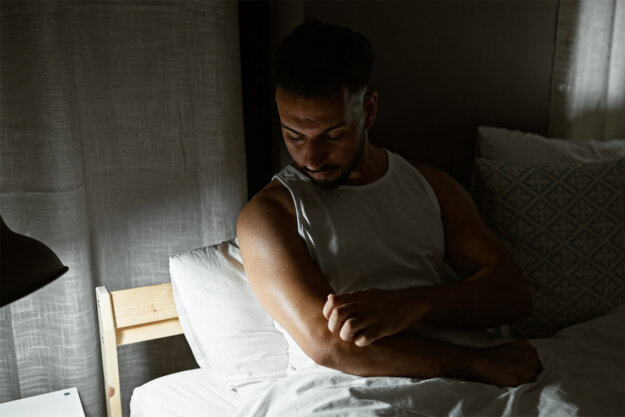 Man in bed scratching meth sores on his arm